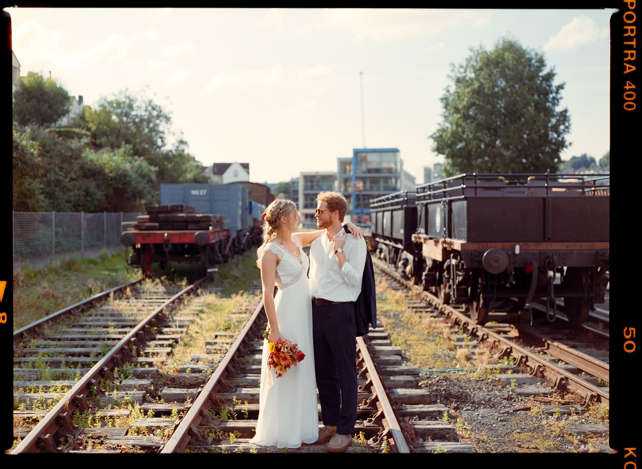 A couple standing on train tracks with vintage railway carriages in the background.