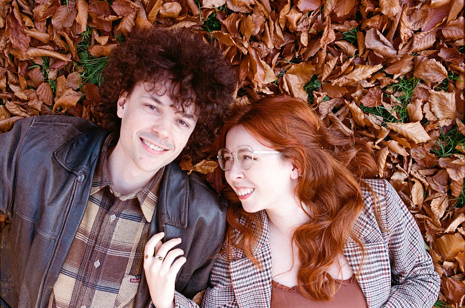 Two people lying on autumn leaves, with heads side by side.