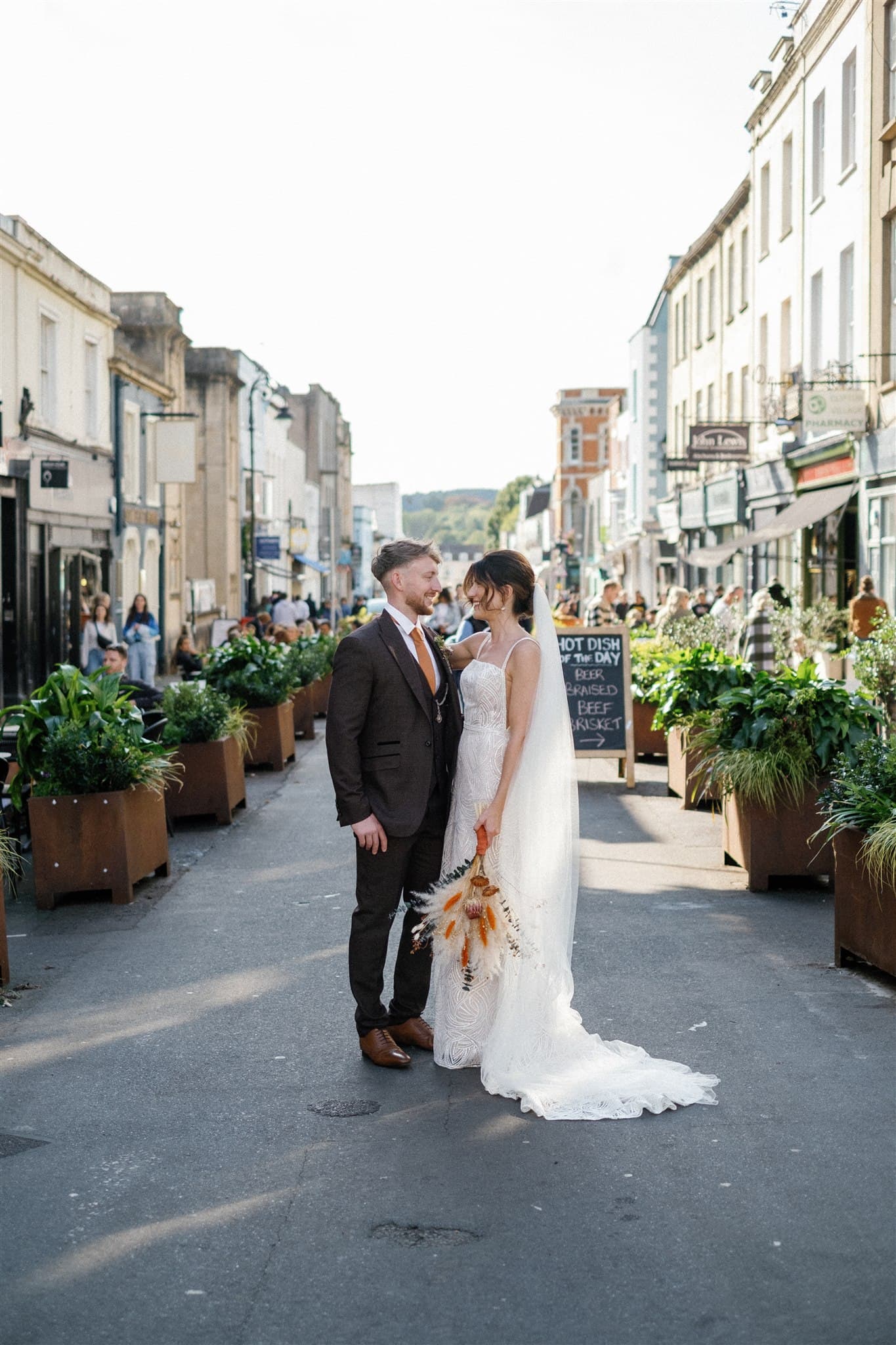 Bride in white dress and groom in suit on a city street with planters.