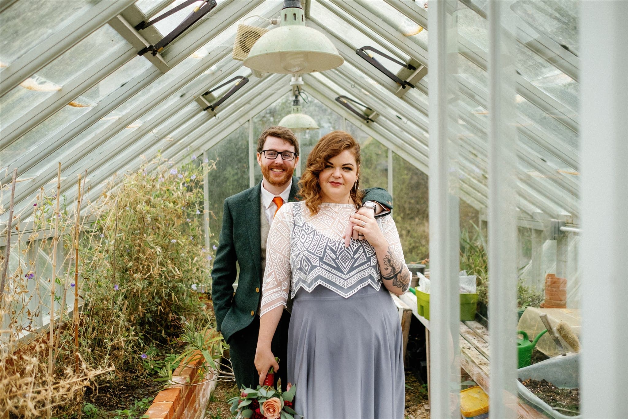 Couple holding hands in a greenhouse surrounded by plants.