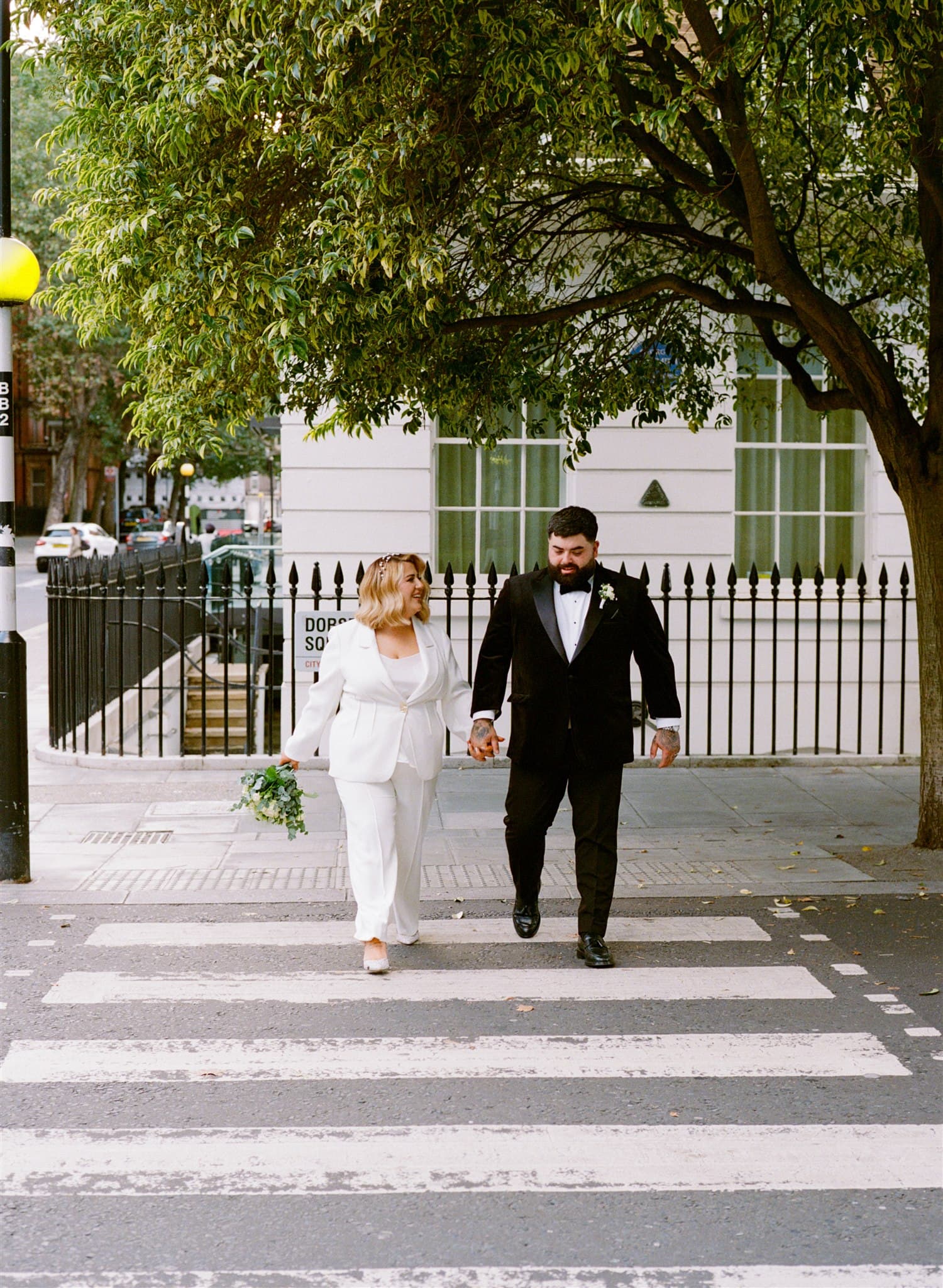 A couple in wedding attire holding hands and crossing the street.